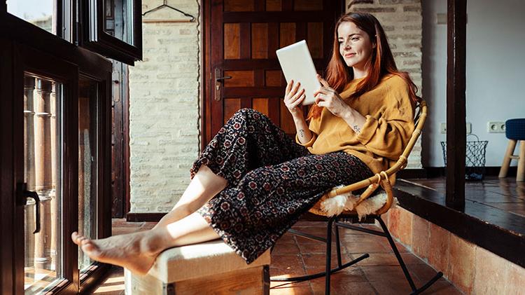 Woman sitting in a chair and researching how to improve financial wellness on her tablet.